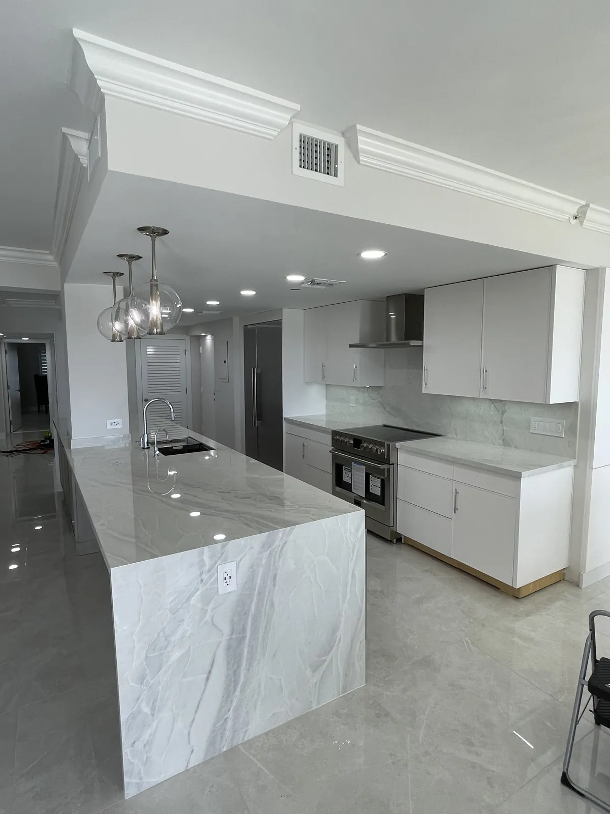 Remodeled kitchen with pendant lights over a waterfall island, stainless range hood and white upper cabinets