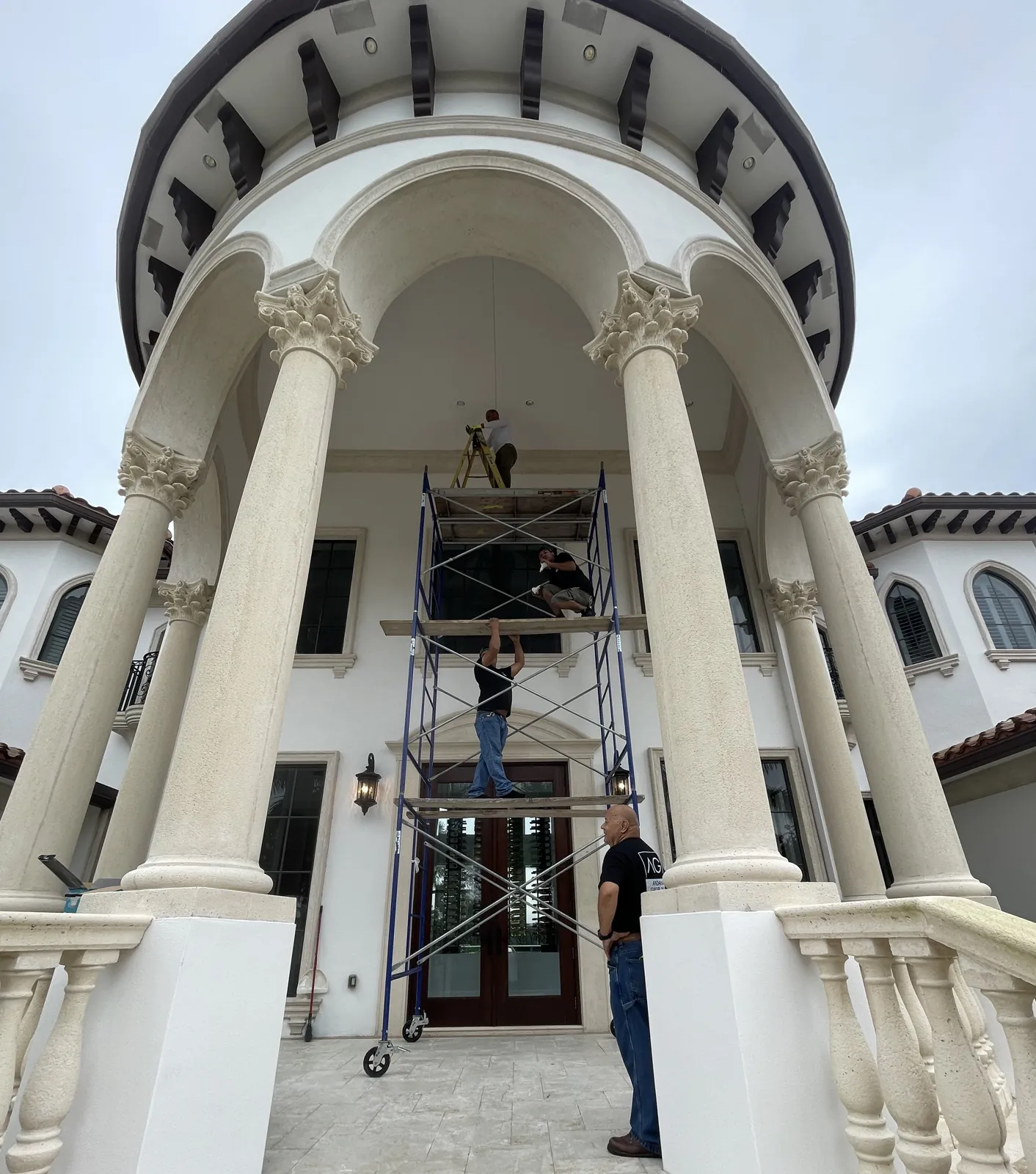 Apadana Group Inc. crew on scaffolding preparing the columns and entry of a Mediterranean-style home for exterior painting