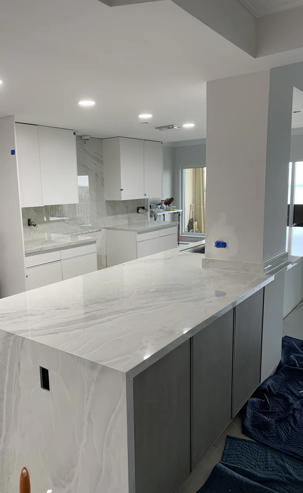 Kitchen remodel in progress with stone island countertop, slab backsplash and white upper cabinets
