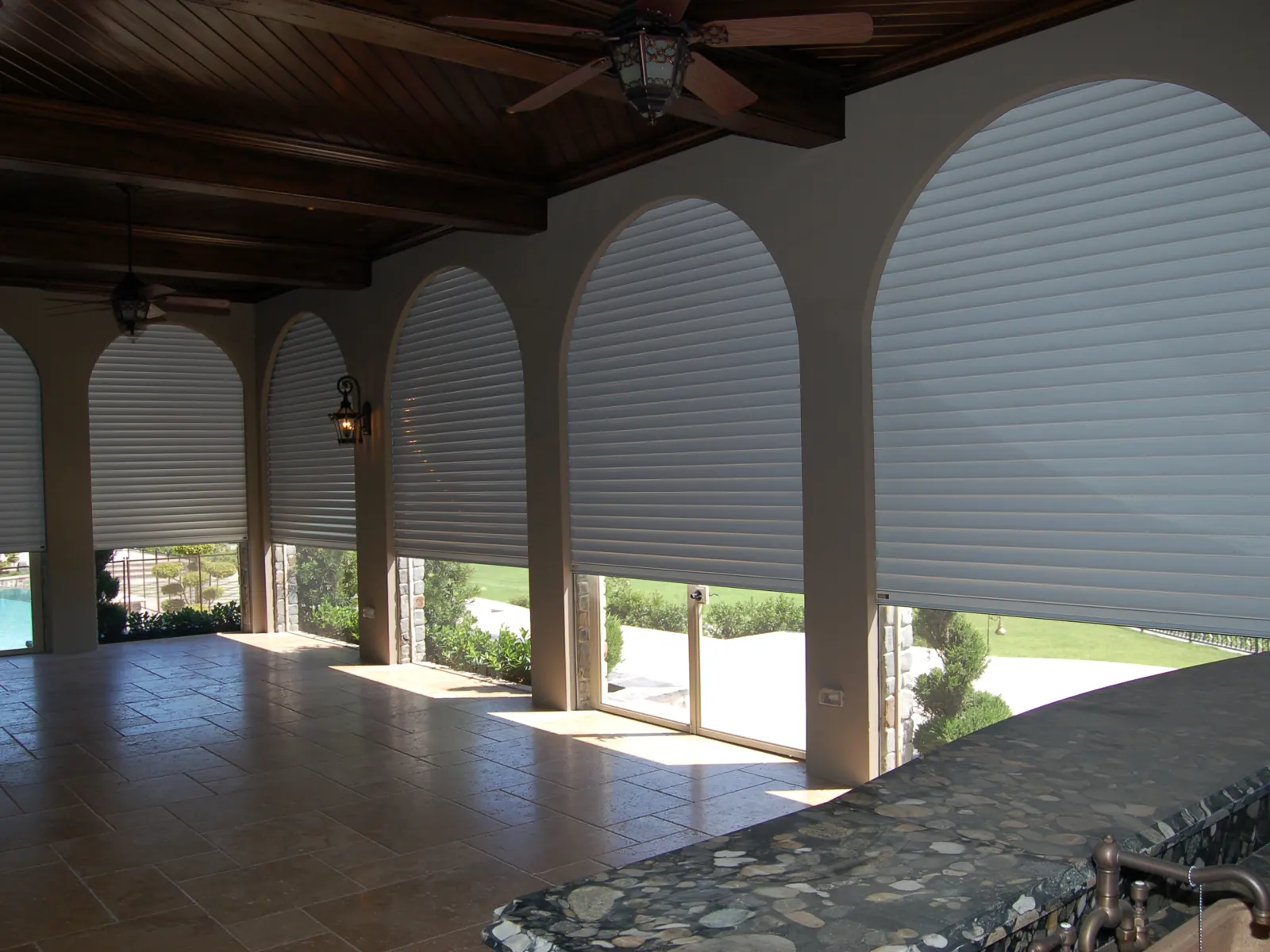 Renovated covered loggia with arched openings, wood plank ceiling and roll-down shutters by Apadana Group Inc.