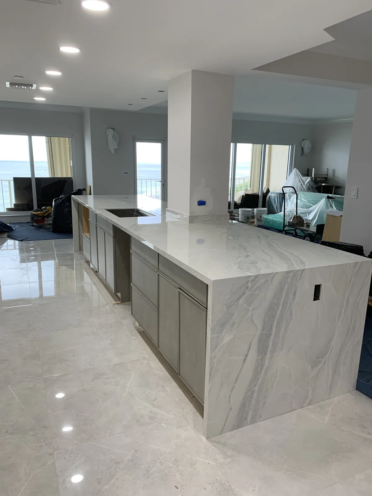 Kitchen remodel with a stone waterfall island, gray base cabinets and porcelain floor tile