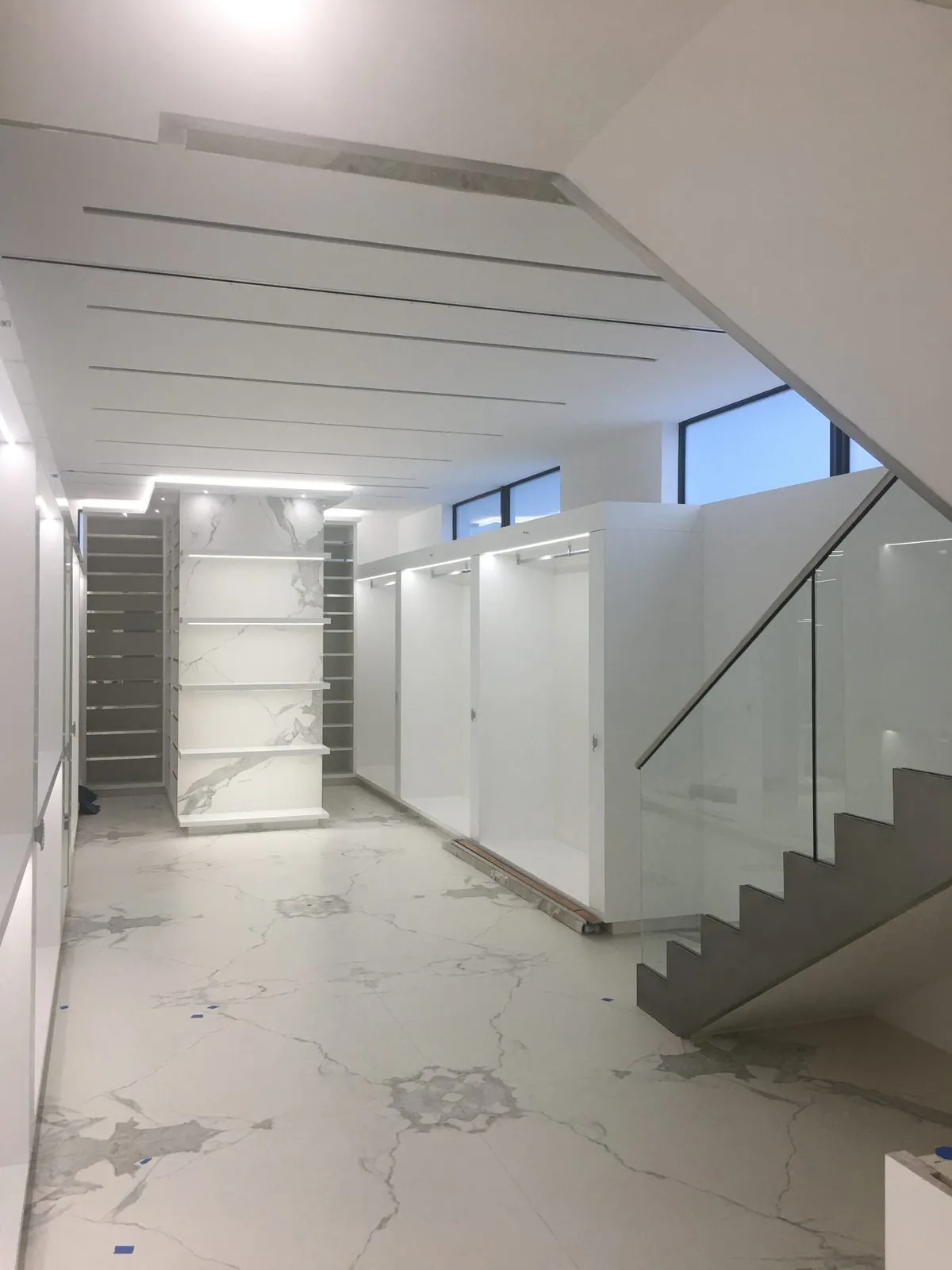 Hallway with glass stair railing, built-in shelving, and linear ceiling lights