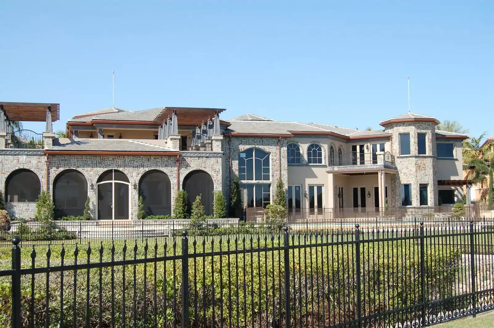 Two-story Mediterranean-style home with stone arches, clay tile roof, and iron fence