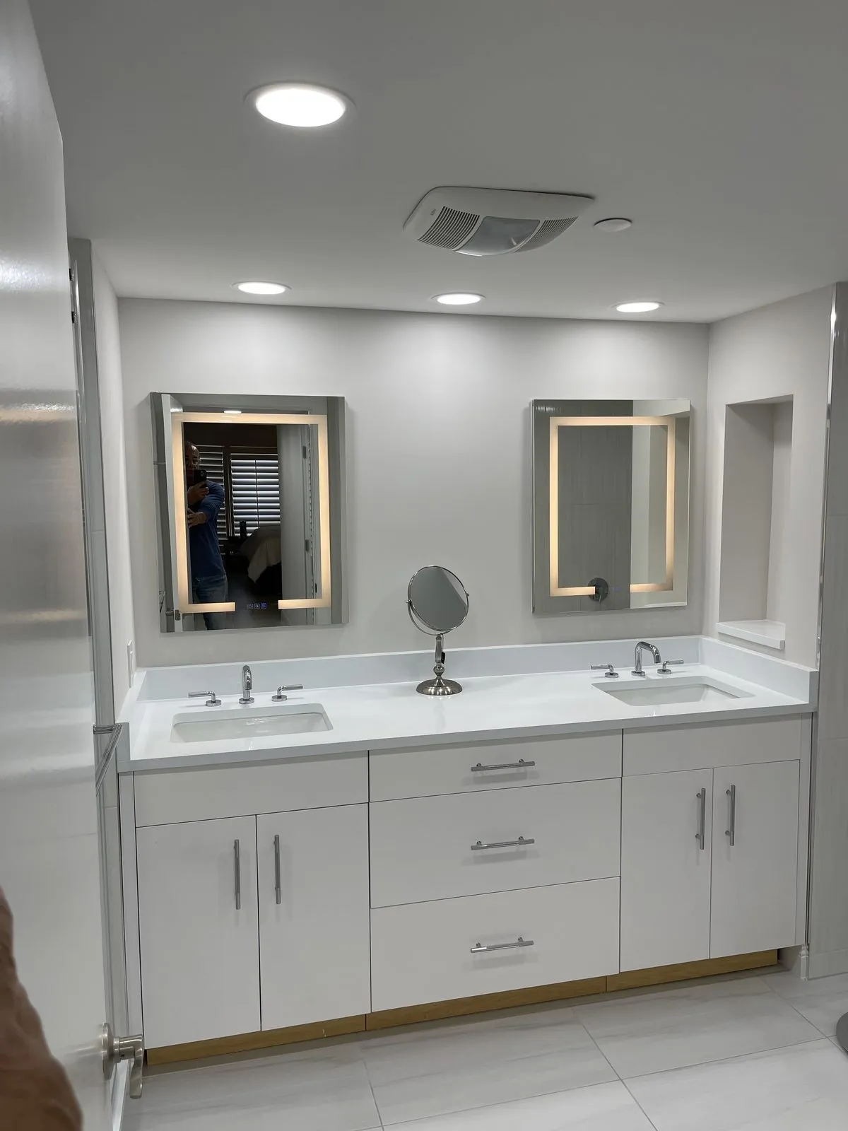 Remodeled bathroom with a white double vanity, two undermount sinks and backlit mirrors by Apadana Group Inc.