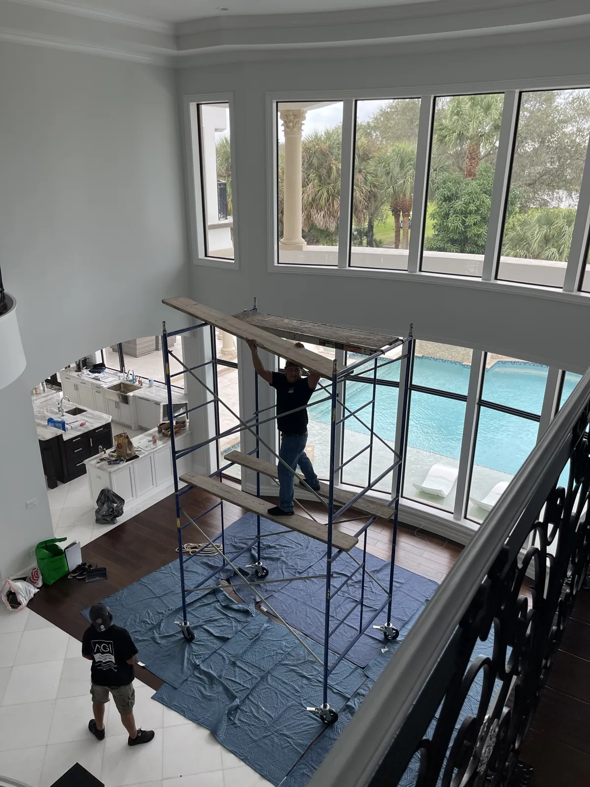 Painter on rolling scaffold in a two-story living room with drop cloths protecting the floor